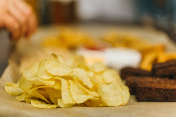 Lager beer and snacks on wooden table. Nuts, chips, peanut, toast, crackers. Appetizer fast food. Craft beer. Beerboard. Tomato cheese and garlic sauce. People dip the appetizer into the sauce.