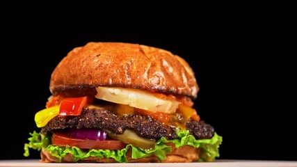 Craft burger is cooking on black background in black food gloves. Consist: red sauce salsa, lettuce, red onion, pickle, cheese, chilli green pepper, air bun and marbled meat beef. Not made ideal
