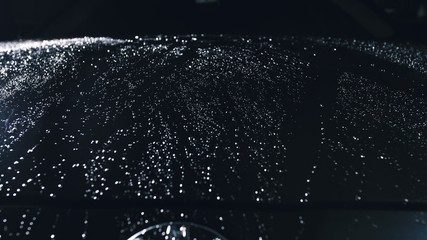 Drop flow down the hood. Close up view of a bonnet car. Dark black cinematic picture. Process stage...
