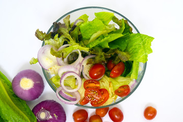 Group of organic vegetable, red onion, tomato, green leaves mixed in glass  bowl isolated on white background