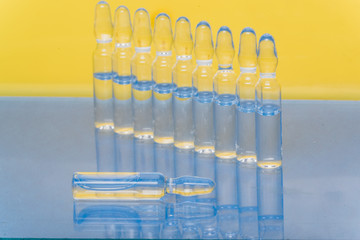 Glass medical ampoule vial for injection. Medicine is liquid sodium chloride with of aqueous solution in ampulla. Close up. Bottles ampule multicolor on background color and water. Human plasma.