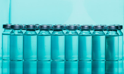 Glass medical ampoule vial for injection. Medicine is liquid sodium chloride with of aqueous solution in ampulla. Close up. Bottles ampule multicolor on background color and water. Human plasma.