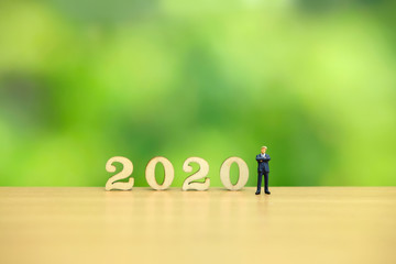 Fototapeta premium Miniature people - businessman greeting for happy new year 2020 with dreamy green background