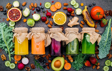Colourful healthy smoothies and juices in bottles with fresh tropical fruit and superfoods on dark...