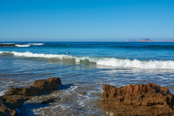 A surfer is floating on a board along the blue waves in white foam. Deep blue water in the atlantic ocean. Shore of the volcanic island of Lanzarote, Canary Islands. February.