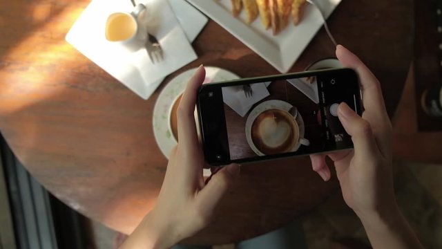 Woman taking photo of coffee by smartphone in cafe.	