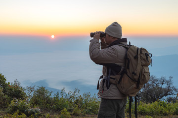 Young man with backpack and holding a binoculars looking on top of mountain