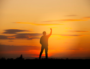 Silhouette of a happy man raised hands up as a successful, victory and achieve a business goal in the sunset sky background.