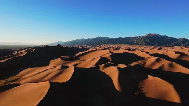 Drone panorama of wavy yellow sand dunes with mountains on the horizon (Great Sand Dunes National Park, Colorado, USA)