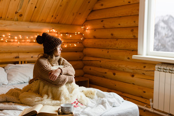 Adult woman relaxing on cozy bed in log cabin in cold winter.