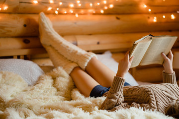 Adult woman relaxing on cozy bed in log cabin in cold winter.