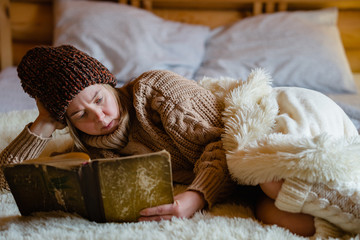 Adult woman relaxing on cozy bed in log cabin in cold winter.