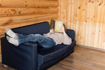 Fototapeta na wymiar Adult woman relaxing on cozy sofa in log cabin in cold winter.