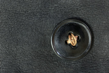 Vintage button. Big black old button with artifacts of time. Roughly sewn with yellow thread to clothes made of natural black suede. Top view.Space for text on the left.