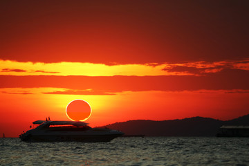 Fototapeta na wymiar phenomenon of partial sun eclipse over silhouette boat on sea and sunset sky