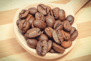 Heap of coffee grains with spoon on wooden board
