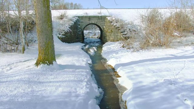 Drone flight down creek, under snow covered railroad tracks, train trestle.