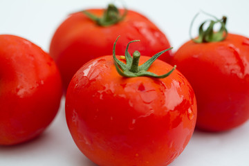 Details of a red tomato with green stipe and other blurry tomatoes in the background