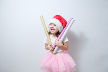 little girl child in a red santa claus hat smiles and holds in her hands rolls of shiny wrapping paper. Preparing for the New Year and Christmas