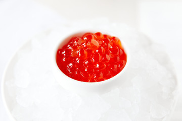 Red caviar, in a white saucer, standing in ice on a white background