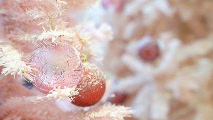Hanging red and pink balls on artificial christmas tree covered with snow.