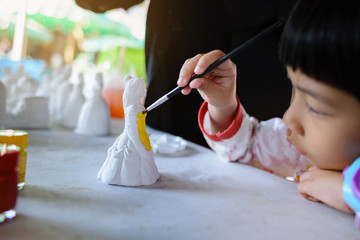 An Asian girl is starting to paint the plaster doll with a poster color. She was staring with...