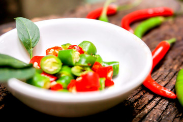 Closeup Red and green chili with chili sliced in the white small bowl on wooden table.