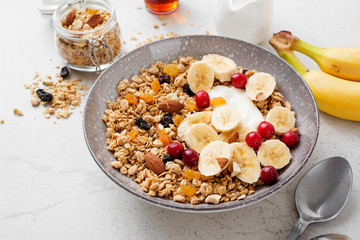Healthy breakfast. Fresh granola, muesli with yogurt banana and cranberry on light gray background.
