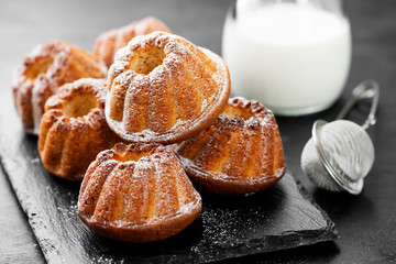 Mini bundt cakes or muffins with icing sugar on black wooden background.