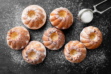 Mini bundt cakes or muffins with icing sugar on black wooden background.