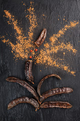 Carob fruit on a black textured background in the shape of an exploding flower.