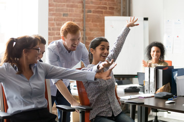 Diverse workers celebrating great news riding on office chairs