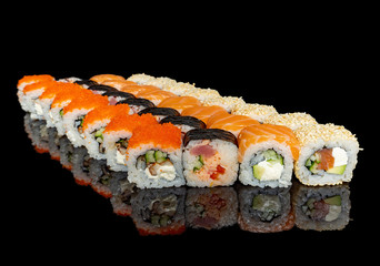 sushi and rolls with different fillings on a black background with reflection