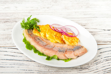 Fermented products in a restaurant close-up. Pickled herring with potato zrazy on a white plate and copy space.