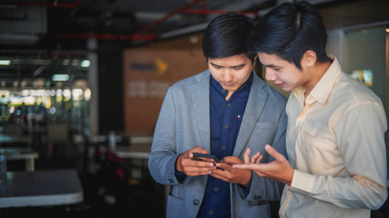 Two young business men are watching something on a mobile phone at work