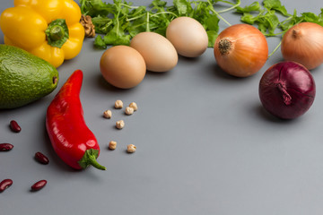 Red and yellow peppers, eggs, onions, chickpeas and beans on a gray background. There is a place for text