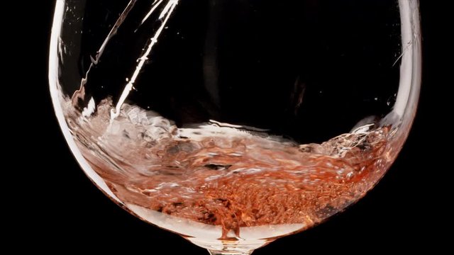 Pink wine is pouring into a glass on a black background. Close shot. Blackmagic 6K camera.