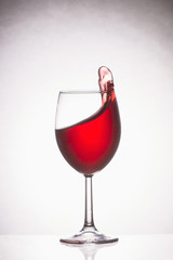 Glass of red wine on a light background, splashing wine