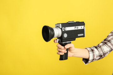 Woman with vintage video camera on yellow background, closeup of hand