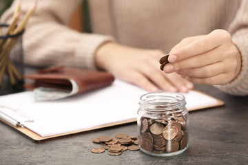 Woman putting money into glass jar at table, closeup