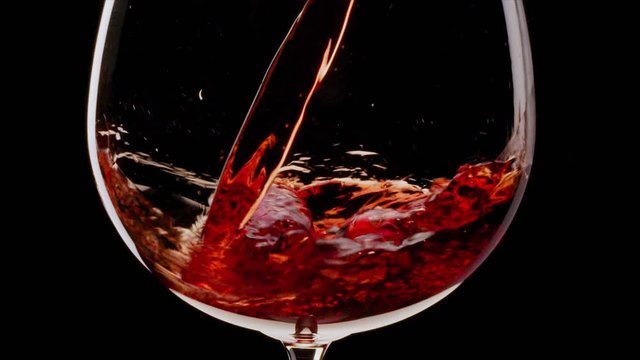 Red wine is pouring into a glass on a black background. Close shot. Blackmagic 6K camera.