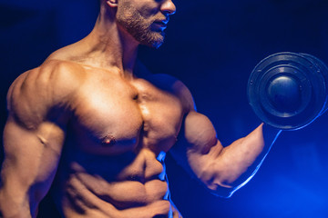 Fototapeta premium Zbliżenie kulturystą lekkoatletycznego mężczyzna przystojny moc robi ćwiczenia z hantlami. Fitness muskularne ciało na ciemnym tle. Zbliżenie