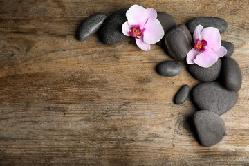 Fototapeta na wymiar Stones with orchid flowers and space for text on wooden background, flat lay. Zen lifestyle