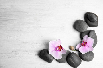 Fototapeta na wymiar Stones with orchid flowers and space for text on white wooden background, flat lay. Zen lifestyle