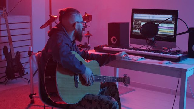 Concept of hobby and making music. Young bearded man plays the guitar in a home music studio