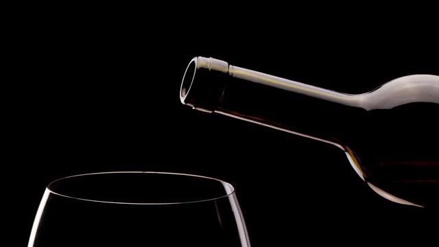Red wine from a bottle pours into a glass on a black background. Close shot. Blackmagic 6K camera.