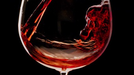 Red wine is pouring into a glass on a black background. Close shot. Blackmagic 6K camera.