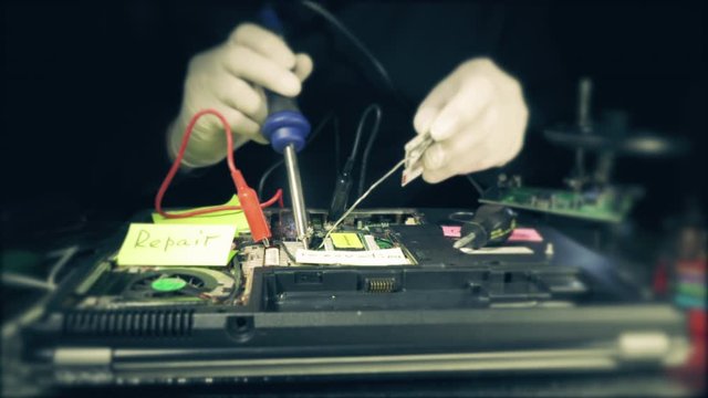 Repairman solders the connectors to the computer circuit Board holding the soldering Iron and piece of tin in hands in the smoke from soldering. Close up