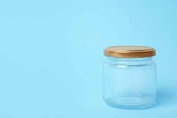Closed empty glass jar on light blue background, space for text