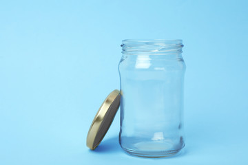 Open empty glass jar on light blue background, space for text